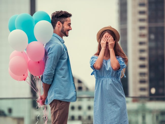 Romantic couple in city with helium balloons as a gift. Balloons are in white blue and pastel pink colours.
