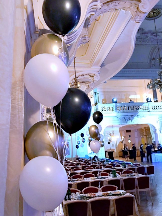 Chromově zlaté, černé a bílé heliové balónky umístěné jako dekorace na mezinárodní konferenci