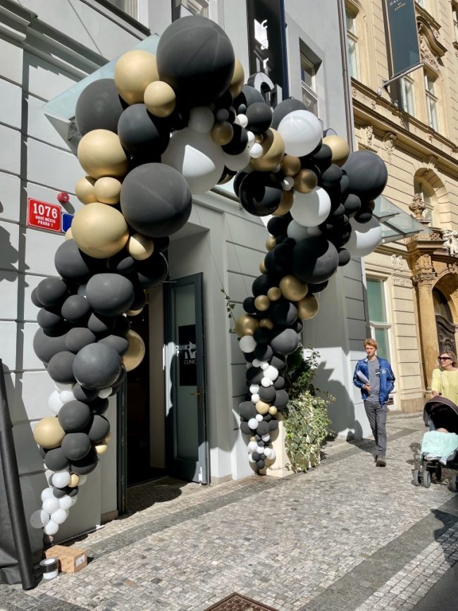 Obrovský balónkový oblouk z černé, zlaté a bílé barvy. Umístěné u vchodu do obchodu