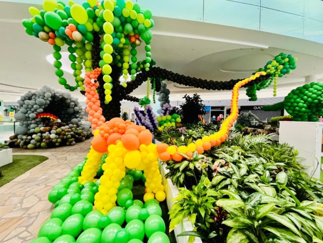 Dinosaurus z balónků oranžovo žlutý s dlouhým ocasem jí strom z balónků na balónkové výstavě