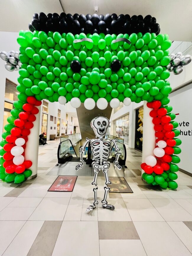 Obří zelená Frankenstein balónková brána s otevřenou pusou a zuby a kostlivcem Náfukou součástí halloweenské balónkové výstavy