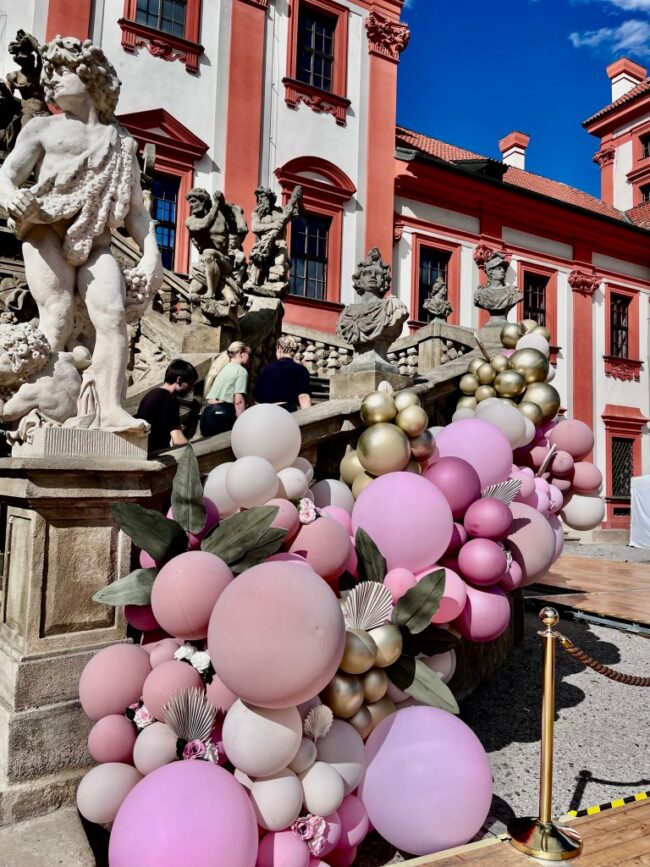 Velká organická girlanda v růžových a fialových barvách umístěna u vstupu do Trojského zámečku.