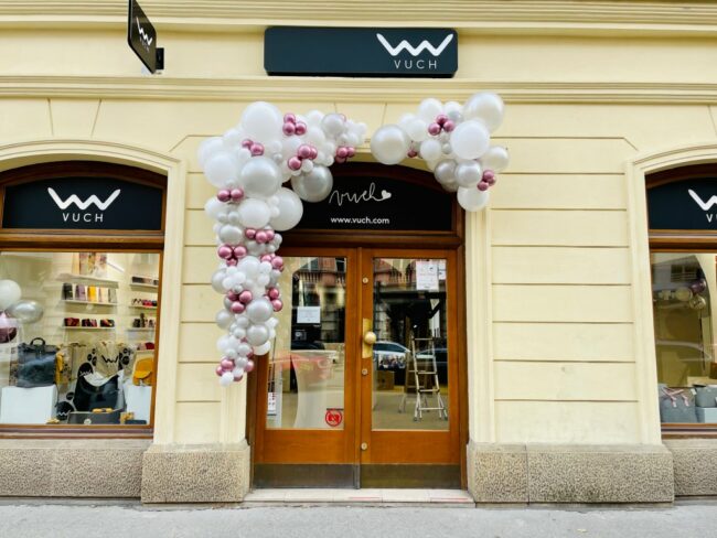 Nepravidelná vstupní girlanda umístěná u vstupu do prodejny Vuch. Balónková dekorace v bílé a fialové barvě.